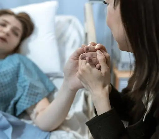 Woman in hospital bed holding hands with another woman